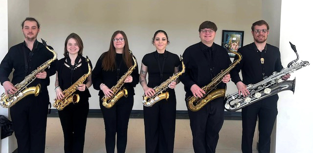 6 students wearing black and holding a saxophone.
