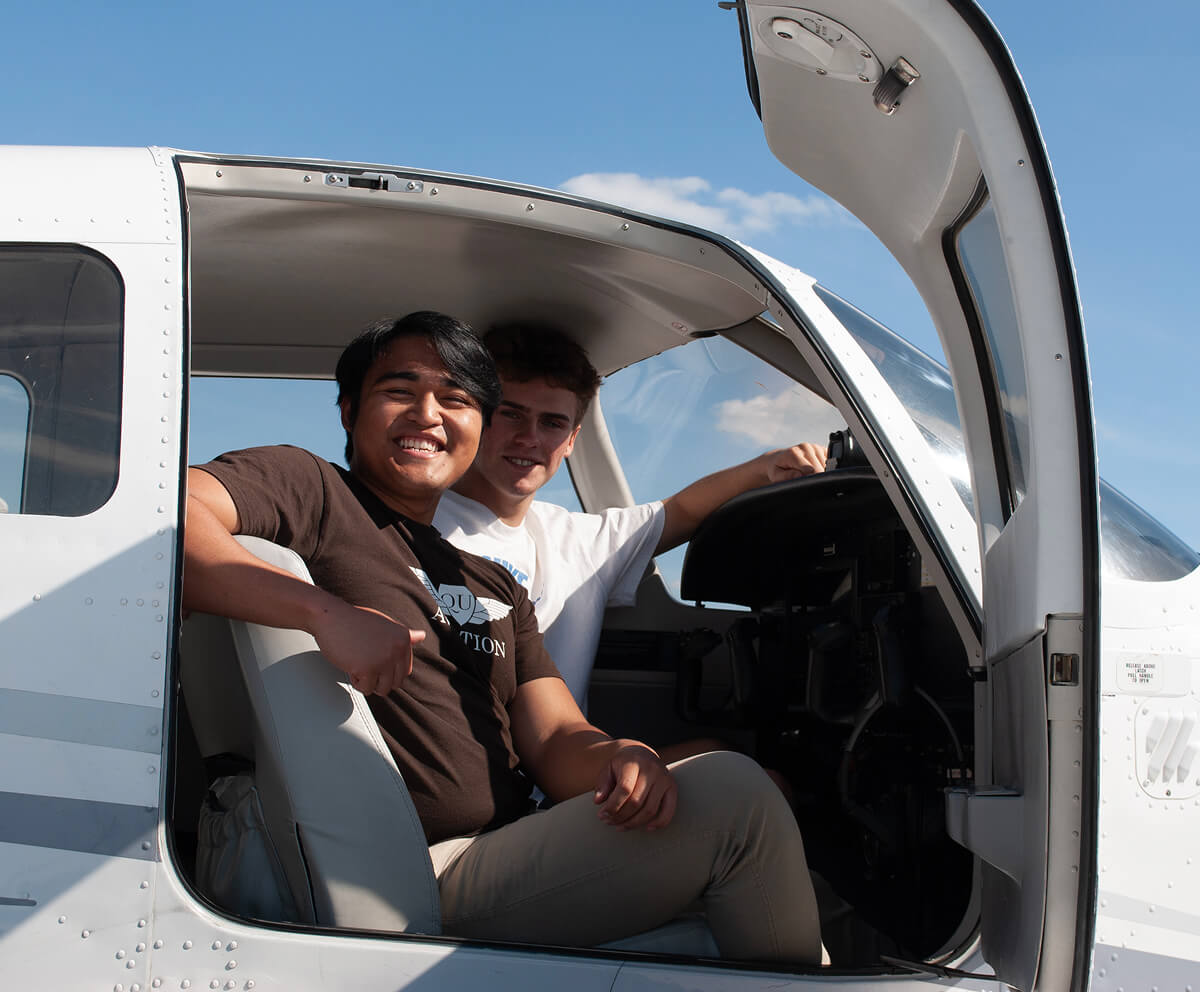 Two flight students inside plane cockpit with door open looking at the camera
