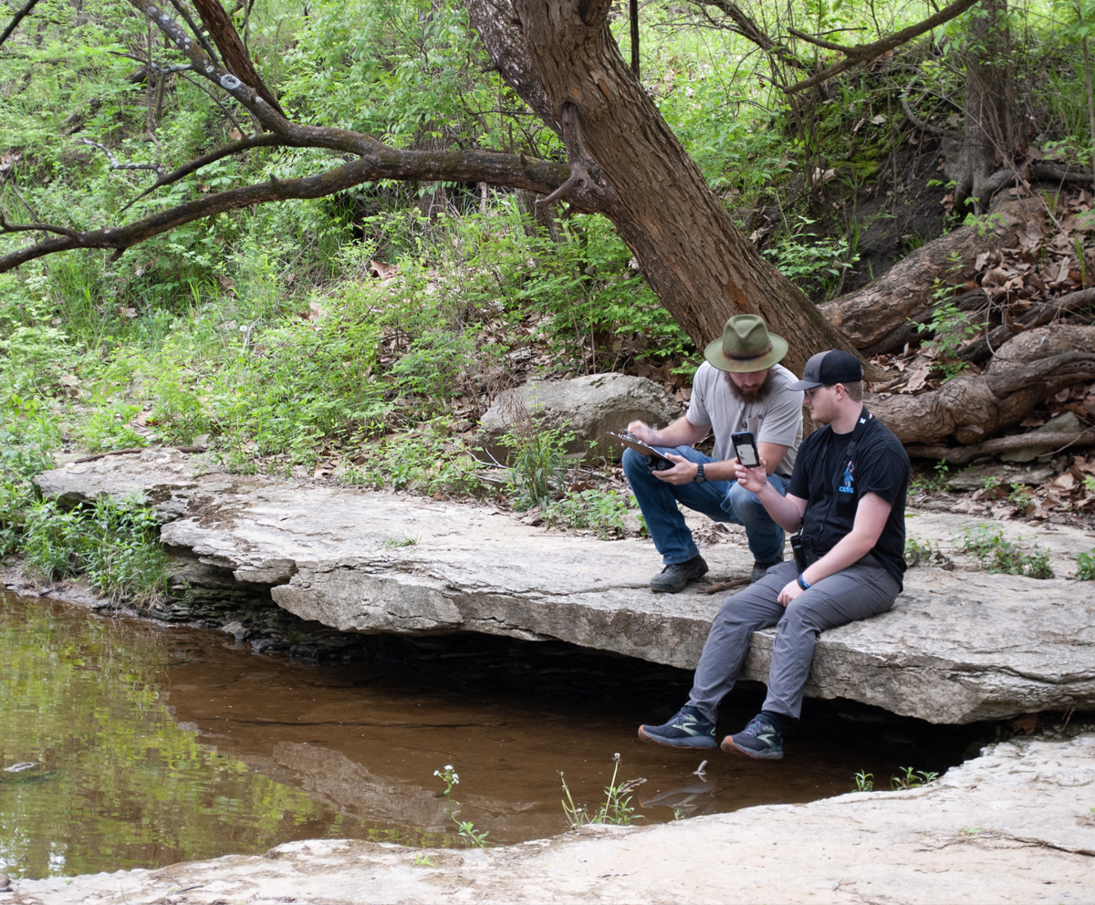 Two students doing biology research near a stream