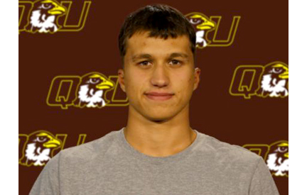 male student in front of QU athletics backdrop with the logo repeated on it.