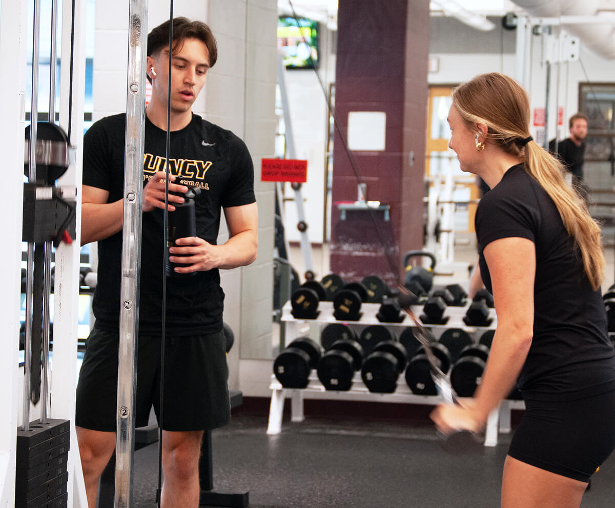 Student in gym working with personal trainer on weights