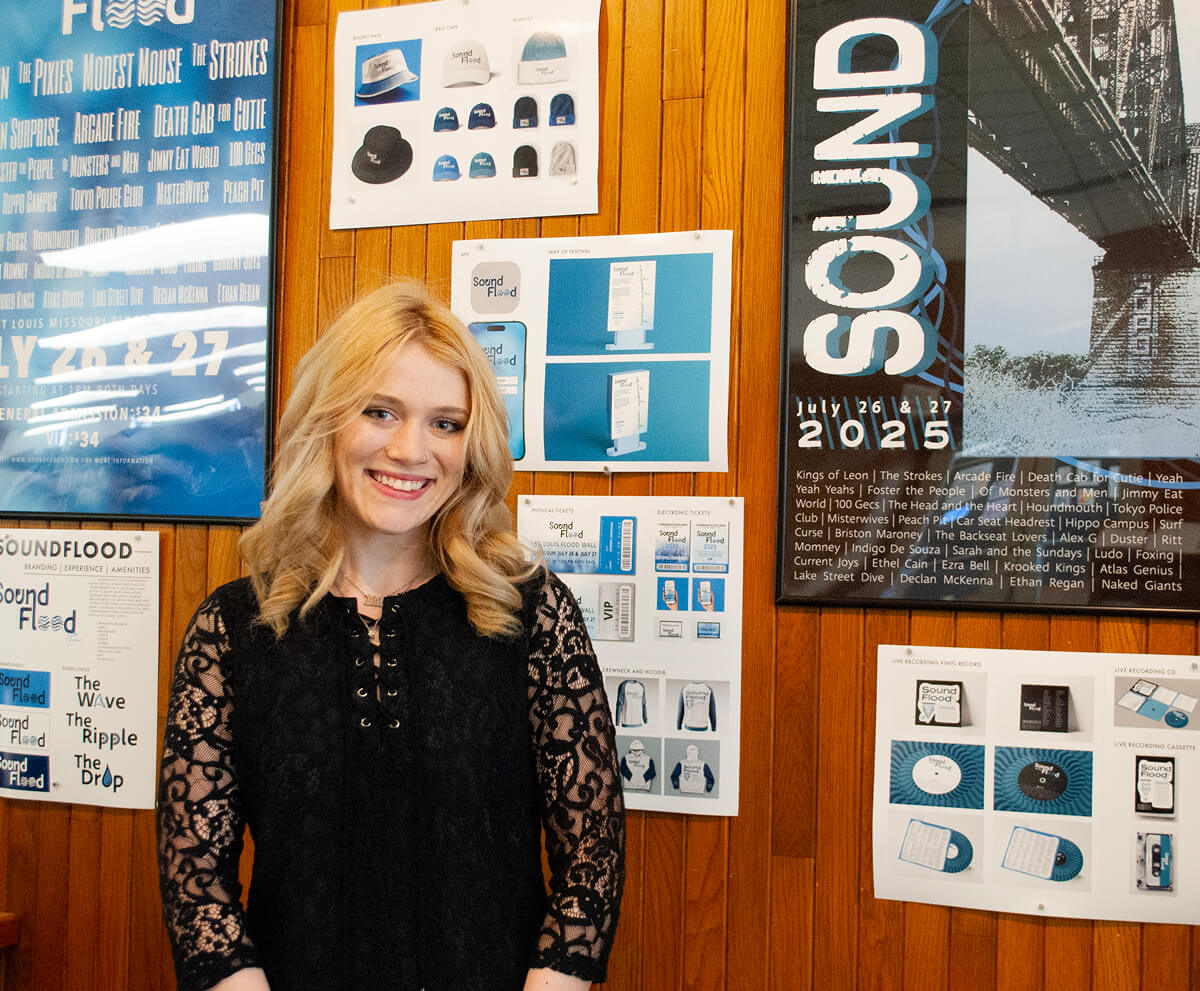 Graphic design student standing next to a wall of posters and branding projects