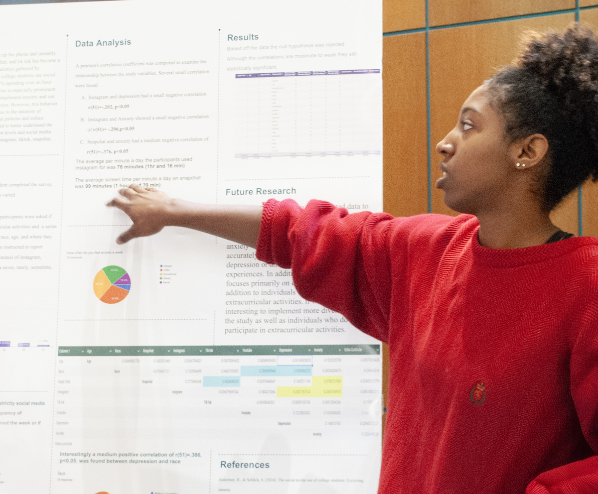 Academic Symposium student pointing to her research on a poster board