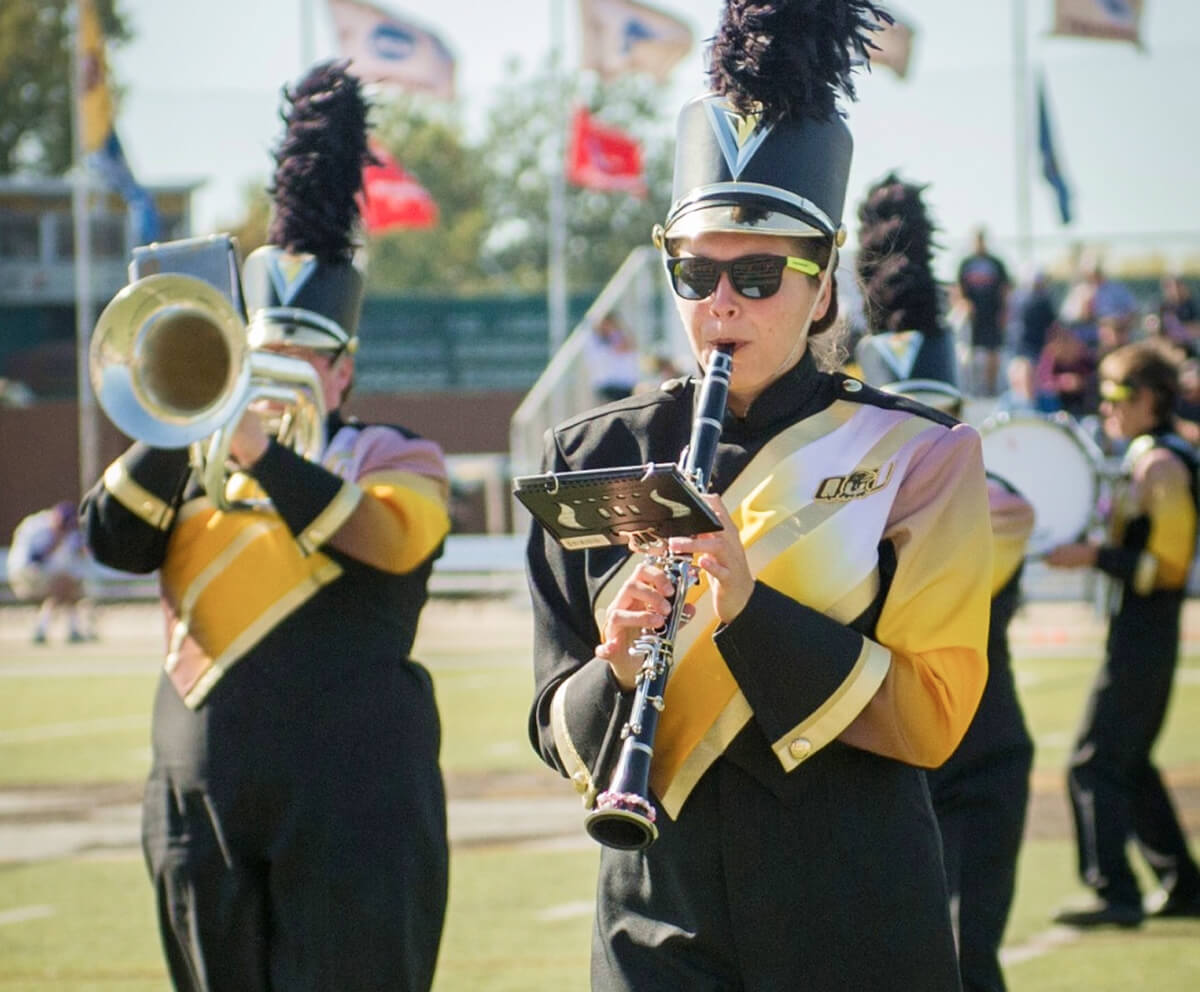 Clarinet player dressed in marching band attire on the field playing with band