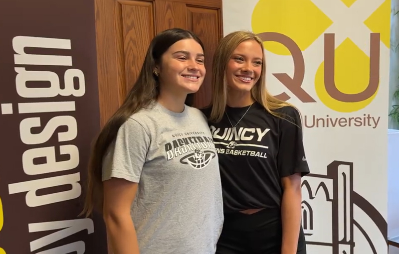 two freshman girls standing for a photo in front of QU backdrop