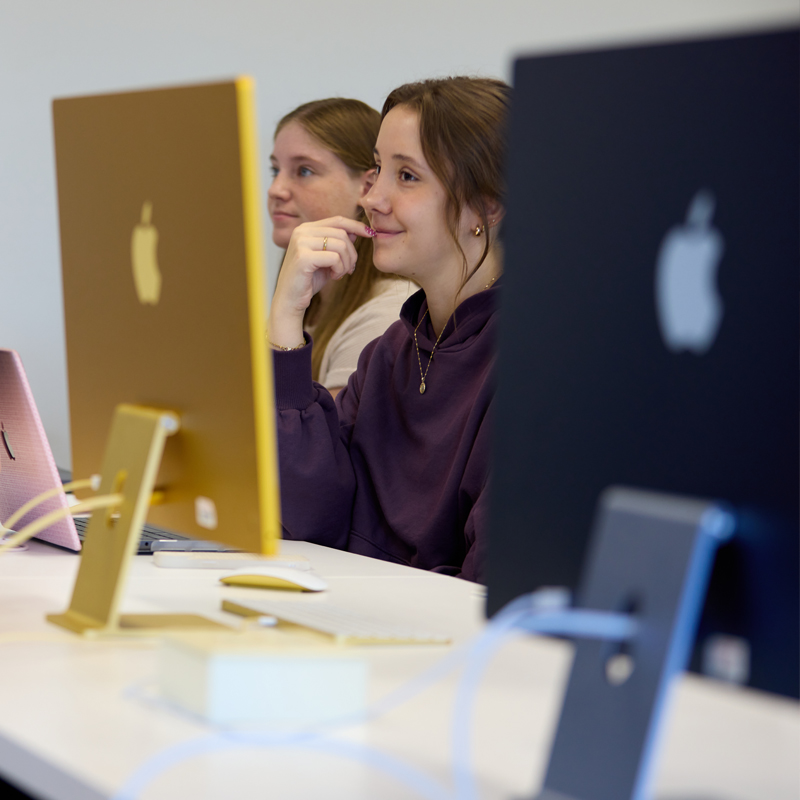 student between to mac monitors in a graphics lab
