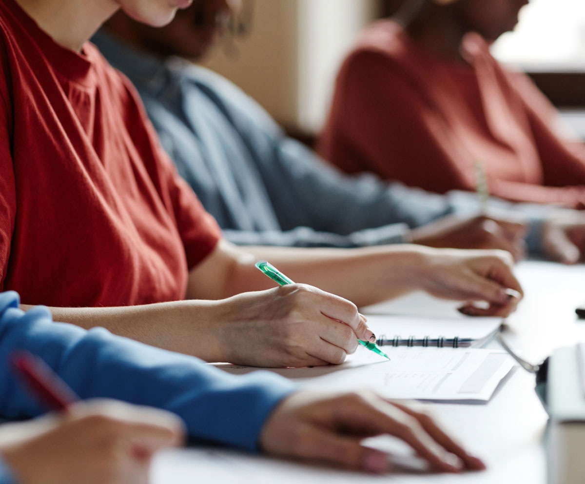 students hands at a desk writing in notebooks