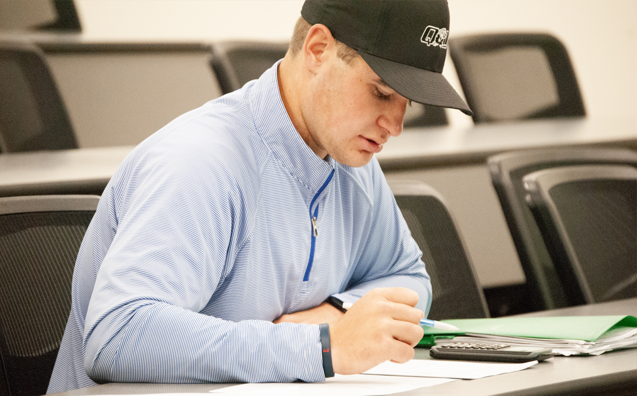 Graduate student writing at a desk in classroom