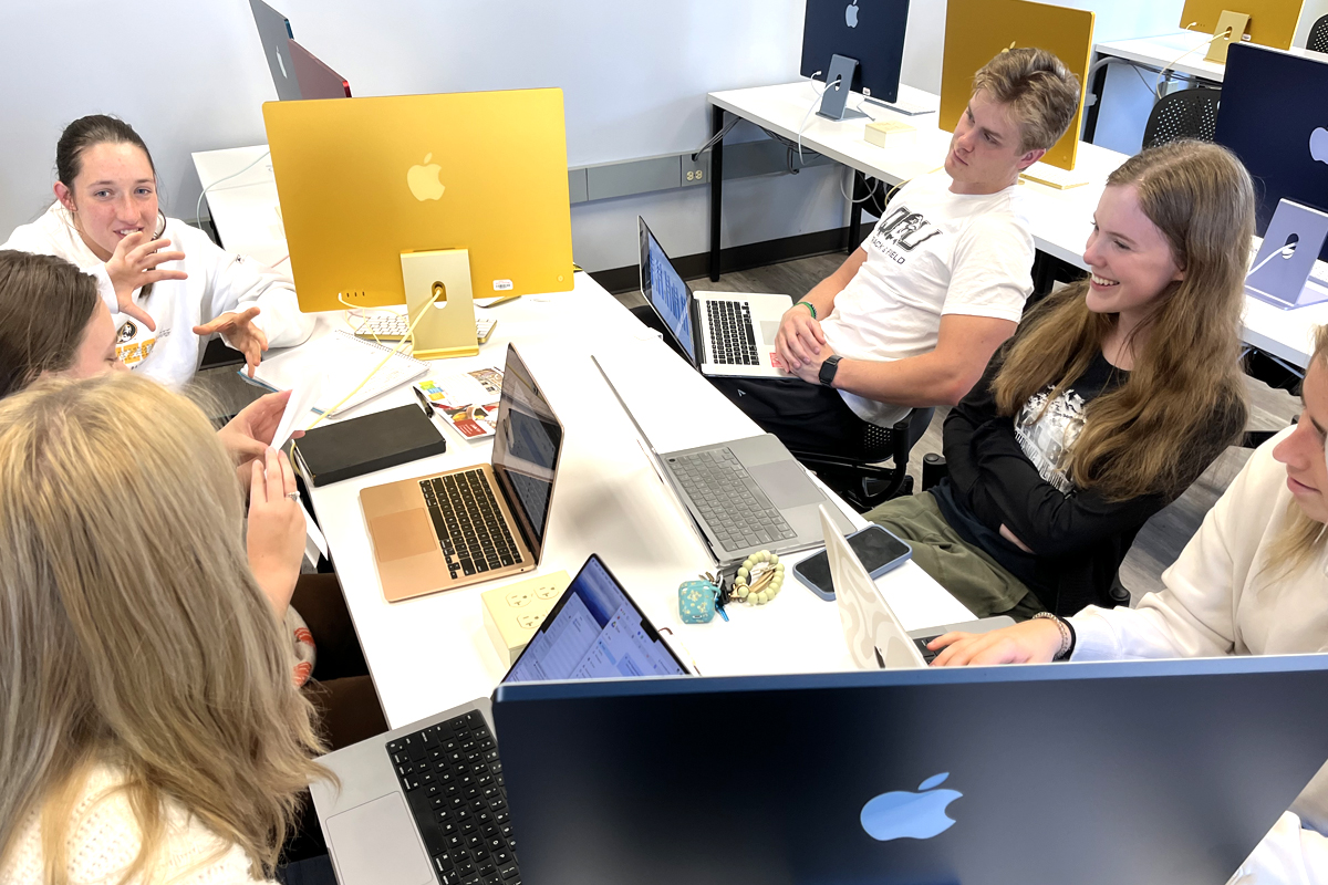 Students sitting with laptops discussing a project
