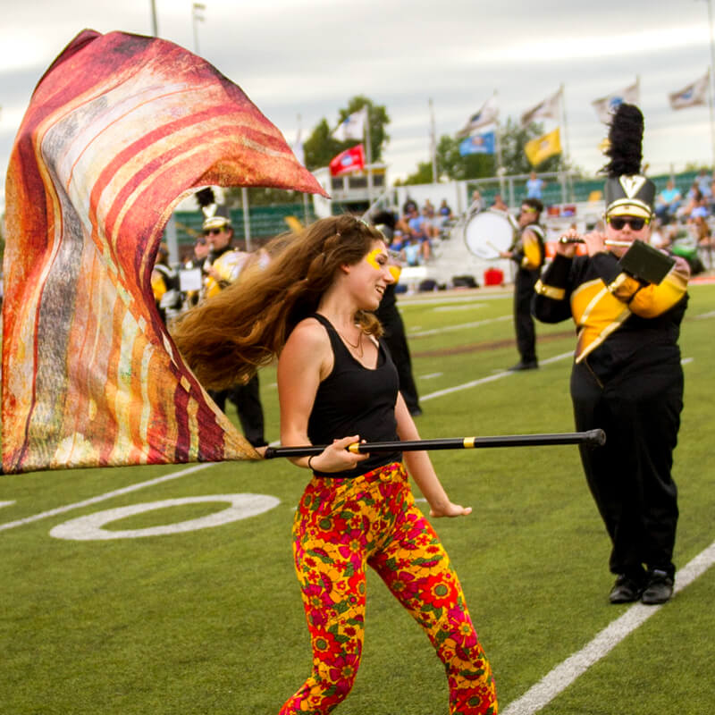 Student twirling flag with marching band on athletic field