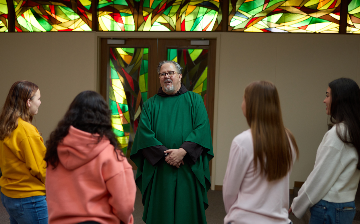 priest in front of stainglass door talking with students