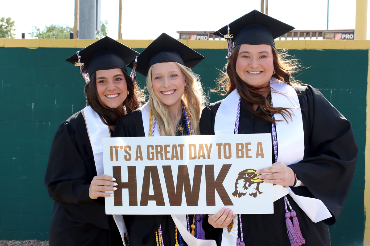 Three female graduates holding a sign at graduation