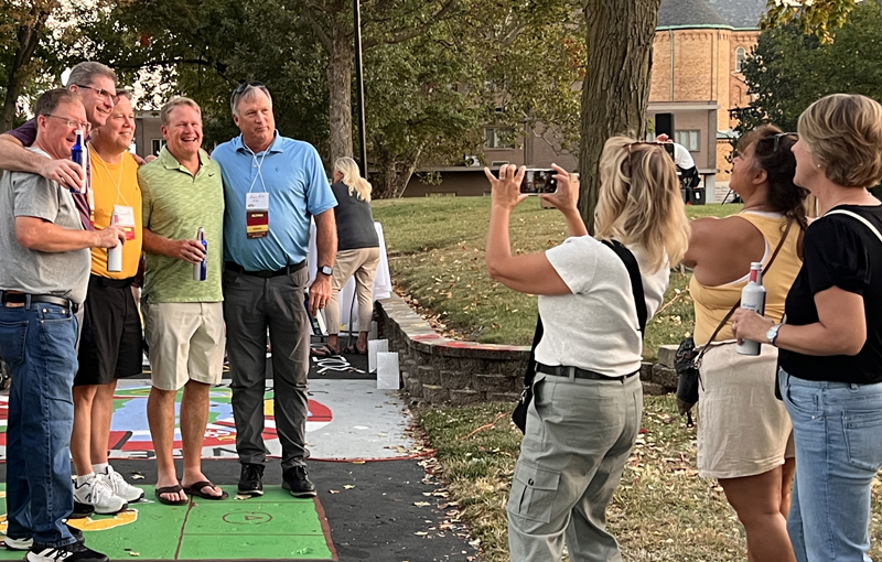 two ladies taking a photo of a group of male alumns at a campus event