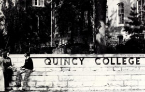 black and white photo of Quincy College sign on stone wall