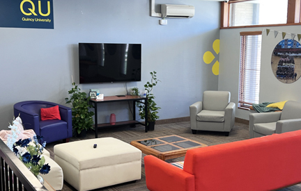 community living room in dorm with red couch, tv on the wall and a few chairs