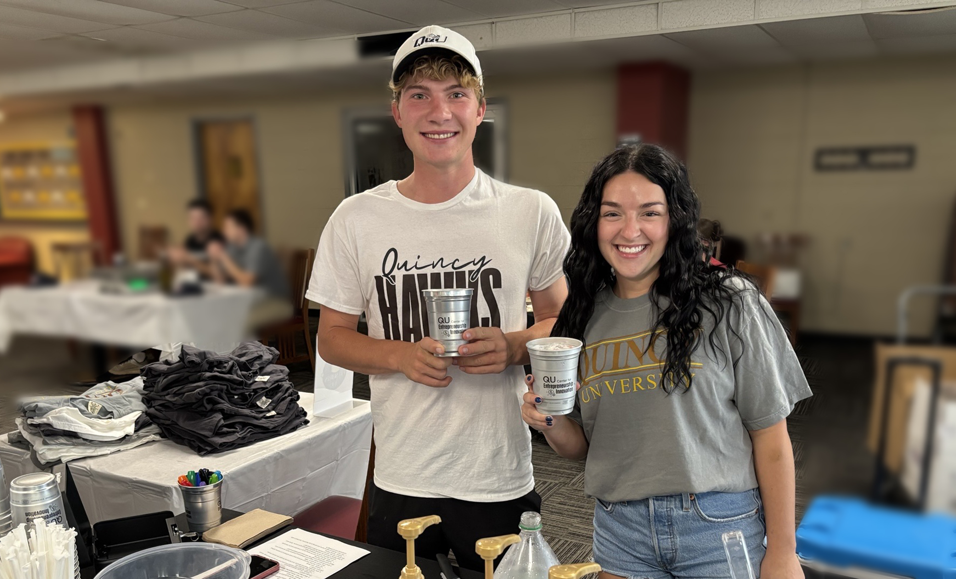 Two students holding up custom cups at a clubs and organizations fair on campus